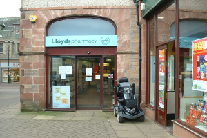 Ein Apothekengebäude mit einem Fahrzeug davor und einem Gebäude links daneben.