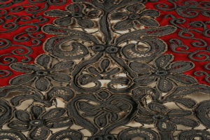 Nahaufnahme eines roten Kleids mit schwarzer Spitzenüberlagerung, das detaillierte Spitzenmuster auf rotem Stoff zeigt.