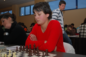 A group of people playing chess, with one person in the center wearing a red dress.