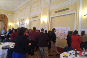 Eine Gruppe von Menschen untersucht Plakate und Diagramme, die an einer Wand in einem scheinbar Kunstmuseum angezeigt werden.