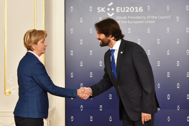 Bundeskanzlerin Angela Merkel und Bundespräsident Joachim Gauck schütteln sich die Hände vor einem Banner mit der Aufschrift "EU-Gipfel", wobei sie freundlich und einladend wirken.