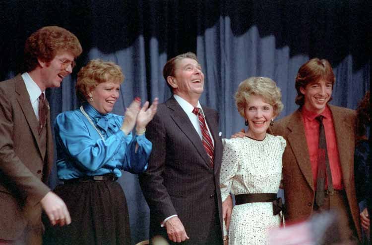 Group of people from *The Brady Bunch* standing on a stage, smiling and clapping with a curtain backdrop.