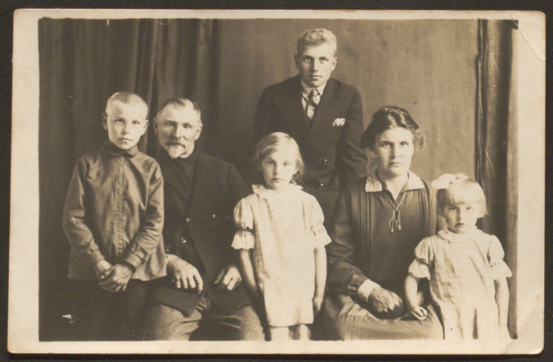 Ein Schwarz-Weiß-Foto einer Familie, die mit einem Mann und einer Frau posiert, die hinter zwei Kindern stehen, und einem Vorhang im Hintergrund.