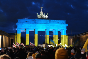 Eine Menschenmenge steht vor dem Brandenburger Tor in Berlin, Deutschland, mit Fahnen und Plakaten in den Händen und einem Banner auf der rechten Seite.