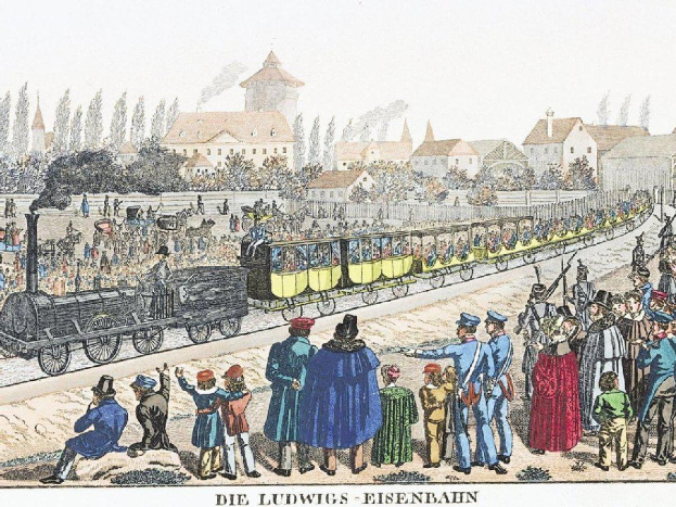 Eine Gruppe von Menschen steht um einen Zug auf einem Gleis herum, einige sitzen im Zug, andere stehen davor, vor Gebäuden und Bäumen, mit dem Text "Ludwigs-Eisenbahn, die erste Bahnstation in Deutschland" unten.