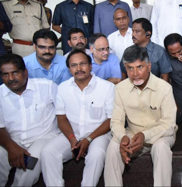 Chandrababu Naidu, Chief Minister of Andhra Pradesh, seated with his cabinet during a public meeting in Hyderabad, with people on stairs and others standing in the background.