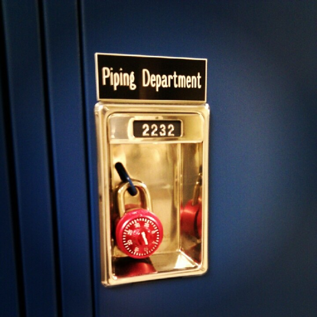 Ein blauer Spind mit einem roten Vorhängeschloss und einer Namensschild mit der Aufschrift "Rohrleitungsabteilung."