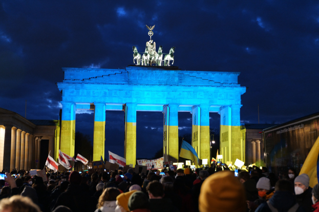 Menschenmenge mit Fahnen und Plakaten vor dem Brandenburger Tor, mit einer Banner auf der rechten Seite des Bildes.