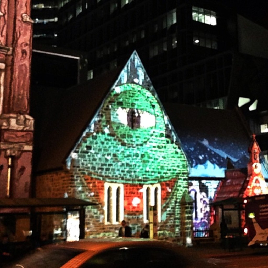 Ein zentrales Haus mit einer Person in der N√§he, flankiert von H√§usern auf beiden Seiten, ein Geb√§ude und Lichter im Hintergrund und ein Auto unten.