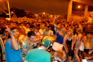 Menschen tanzen im Vordergrund auf einem Konzert mit Lichtern, Polen, Bäumen und anderen Gegenständen im Hintergrund.