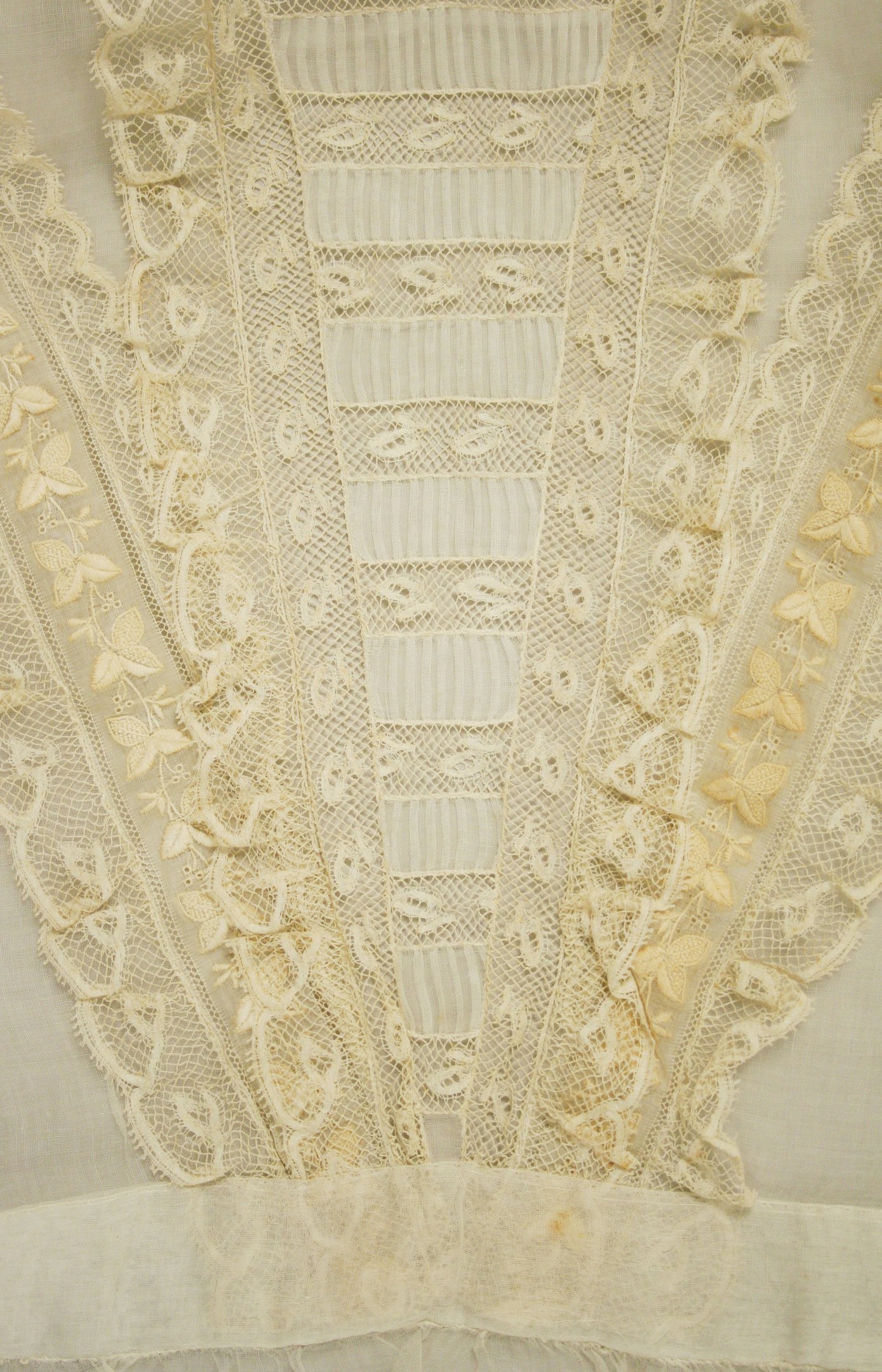 Nahaufnahme eines weißen Kleides mit zarten, detailreichen Spitzenverzierungen auf einem leichten, luftigen Stoff.