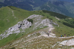 Gruppe von Menschen beim Wandern auf einem Berghang mit grünem Gras und steinigem Gelände, Himmel im Hintergrund sichtbar