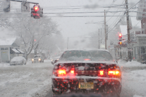 Eine schneebedeckte Straße mit spärem Fahrzeugverkehr, gesäumt von schneebedeckten Bäumen und Häusern auf beiden Seiten.