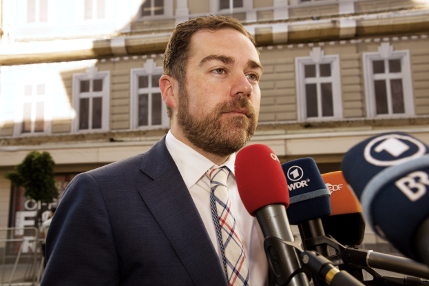 Ein Mann in Anzug und Krawatte spricht vor einem Gebäude zu den Medien, wahrscheinlich wegen einer dreijährigen Haftstrafe.