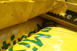 Ein Haufen gelber Plastiktüten mit verschiedenen Gegenständen, darunter Obst, Gemüse und Snacks, mit darauf gedrucktem Text.