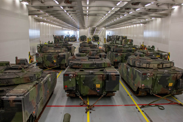 Ein grosser Militaraerraum mit zahlreichen in Reih und Glied aufgestellten Panzerkaempfern, beleuchtet von Deckenleuchten.