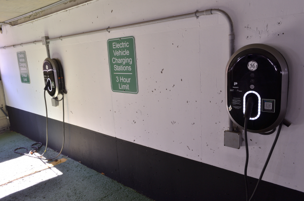 Eine Elektrofahrzeug-Ladestation in einer Tiefgarage mit zwei Ladesäulen an der Wand und Schildern mit Text darauf, der Boden ist unten im Bild sichtbar.