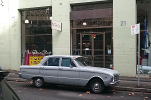 Ein silbernes Auto steht vor einem Gebäude mit mehreren Türen auf der Straße, und ein Schild ist an einem nahen Pfahl zu sehen.