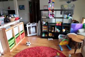 Ein Innenblick in ein Haus mit einem Regal voller Spielzeuge, einem Tisch, einem Ball und einer Küchentheke.