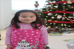 Ein Mädchen lächelt vor einem Weihnachtsbaum und einem Fenster, mit einem Buch vor dem Baum.