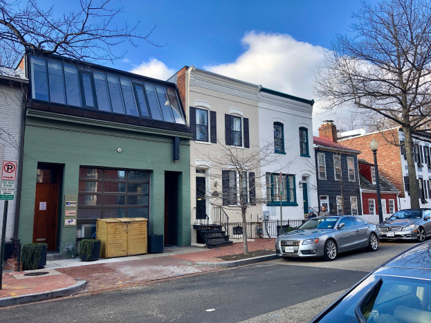 Eine Straße mit parkenden Autos, Gebäuden, Bäumen, Laternen, Schildern und Holzboxen unter einem bewölkten Himmel in einem Philadelphia-Viertel.