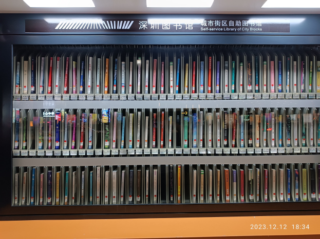 Eine hell erleuchtete Bibliothek mit hohen Bücherregalen voller Bücher, mit einer Texttafel und einem Wasserzeichen unten, ähnlich einer Selbstbedienungsbibliothek in Stadtblöcken.