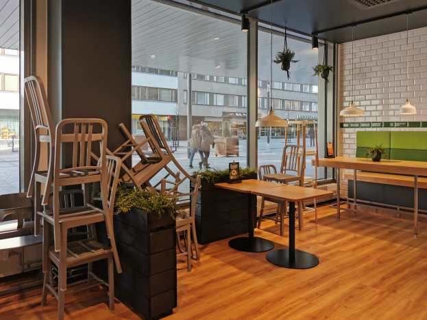 Innenansicht eines Restaurants in Berlin mit Holztischen und -stühlen in der Nähe eines großen Fensters, das Fußgänger, Gebäude und Straßenelemente zeigt.