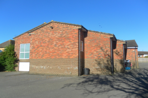 Rote Backstein-Semi-Detached-Bungalow mit weißer Tür und Fenstern, gelegen auf St Johns Road, St Johns Wood, Luton, umgeben von Bäumen und Mülltonnen, mit Himmel im Hintergrund.