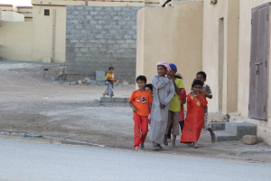 Eine Gruppe lachender Kinder im Freien mit Gebäuden, Wasser, Felsen und einer Straße im Hintergrund.