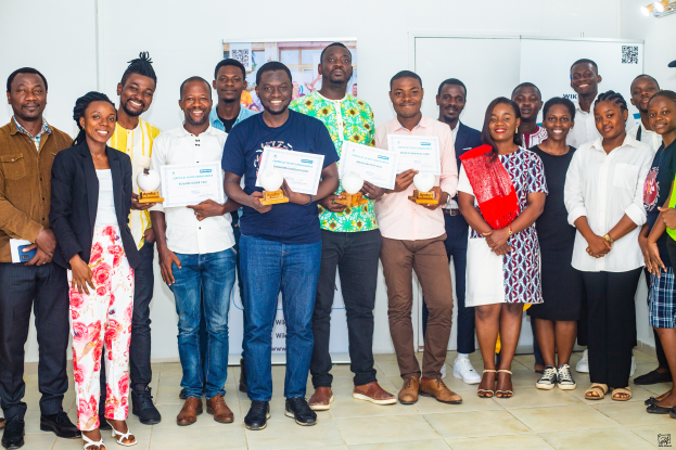Eine Gruppe strahlender Menschen hält Zertifikate in der Hand und steht zusammen in einem Raum, mit einem Tisch voller Gegenstände rechts und Tafeln und einem Plakat im Hintergrund, feiert die WIK Awards 2019.