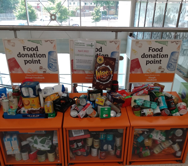 Orange Schübe mit Lebensmitteln wie Flaschen, Dosen und Kartons, neben Texttafeln, mit Blick auf Fahrzeuge, Bäume, Gebäude und Himmel durch Glasfenster.