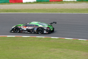 Ein Sportwagen mit Text und Zahlen, der an den 24 Stunden von Le Mans teilnimmt, fährt auf einer Rennstrecke mit Gras auf beiden Seiten und einer Wand im Hintergrund.