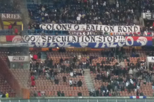 Ein Stadion voller Menschen, Fahnen und Stühle, mit einem Zaun unten und einer Treppe links.