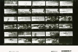 Schwarzes und weißes Foto eines konzentrierten Mannes in einem weißen Hemd und Shorts, der Tennis spielt und einen Schläger hält, mit einem Filmstreifen im Hintergrund.