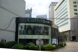 Ein Geschäftsgebäude mit ein paar Pflanzen davor, umgeben von vielen hohen Gebäuden im Hintergrund, mit einigen Drähten sichtbar.