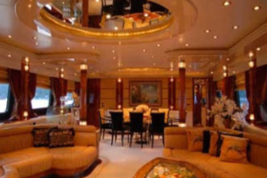 Ein Hotellobby mit Sofas, Kissen, Stühlen, Tischen, Blumenvasen und Blumen im Vordergrund; Fenster, Vorhänge und Lampen auf der linken und rechten Seite; eine Leuchte und ein Rahmen im Hintergrund; und ein Spiegel mit Deckenleuchten oben.