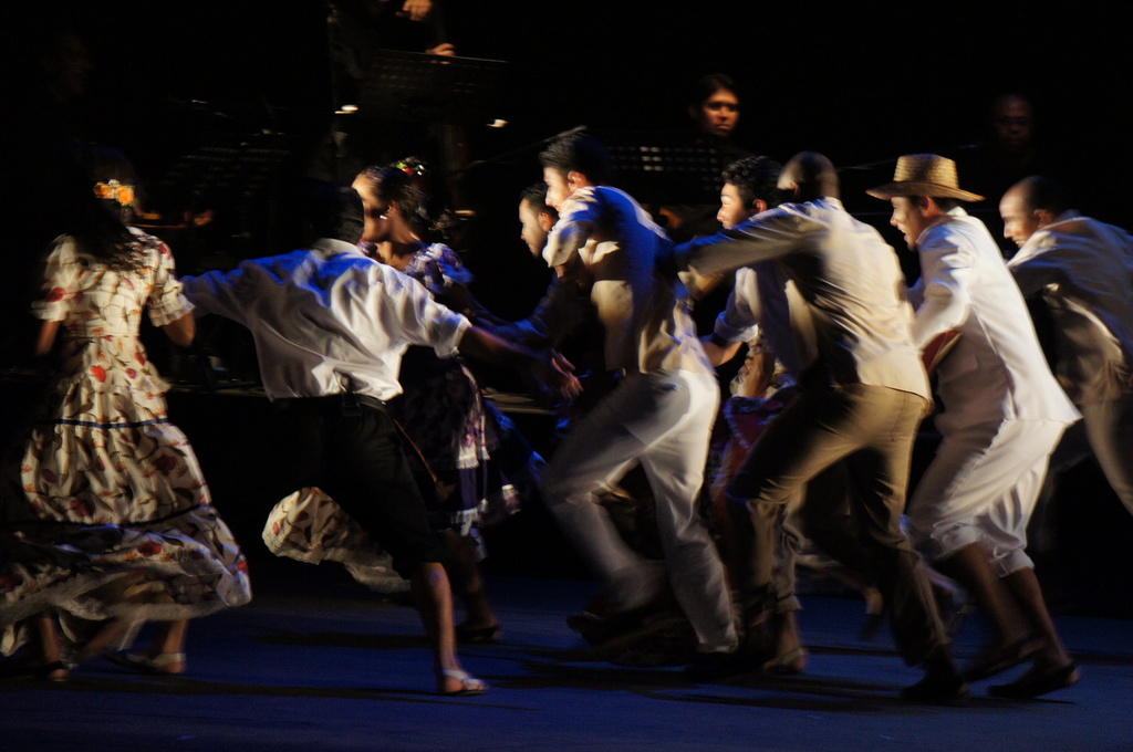 Eine Gruppe von Menschen tanzt mit anderen und Equipment im Hintergrund.