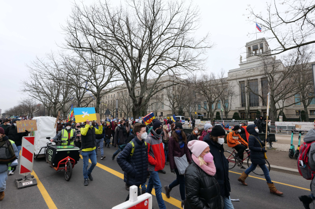 Eine große Gruppe von Menschen nimmt an einer Protestkundgebung in Washington, D.C. am 21. Januar 2020 teil und marschiert eine Straße entlang mit Schildern, Bannern und Fahrrädern, vor einem Gebäude mit Schautafeln, Bäumen und einem klaren blauen Himmel.