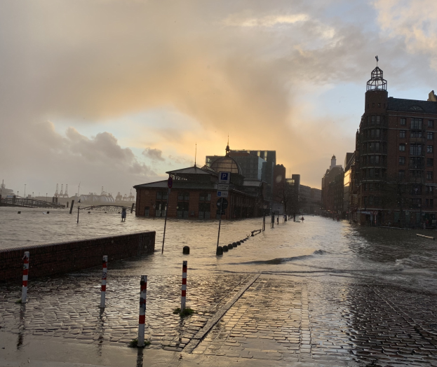 Uberflutete Straße in Hamburg, Deutschland mit Wasser, das die Straße, Masten, Schilder, Gebäude und eine Brücke bedeckt.