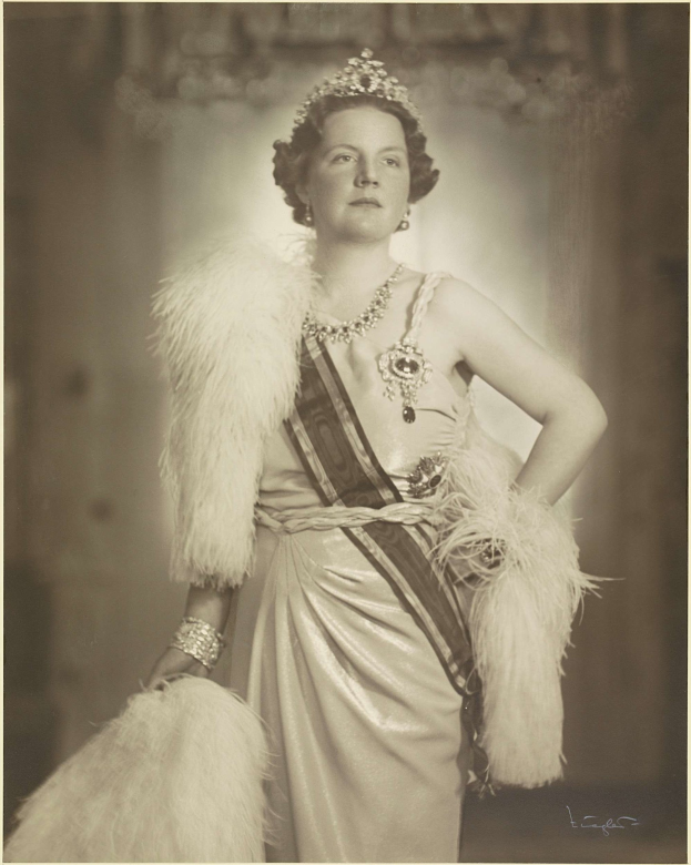 Schwarz-weiß-Foto der Queen Elizabeth II in einem Kleid und einer Krone, mit unscharfem Hintergrund und Text unten.