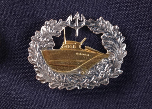 Ein gold-silbernes Abzeichen mit einem Boot, das die deutsche Marine darstellt, auf einem Tuch.