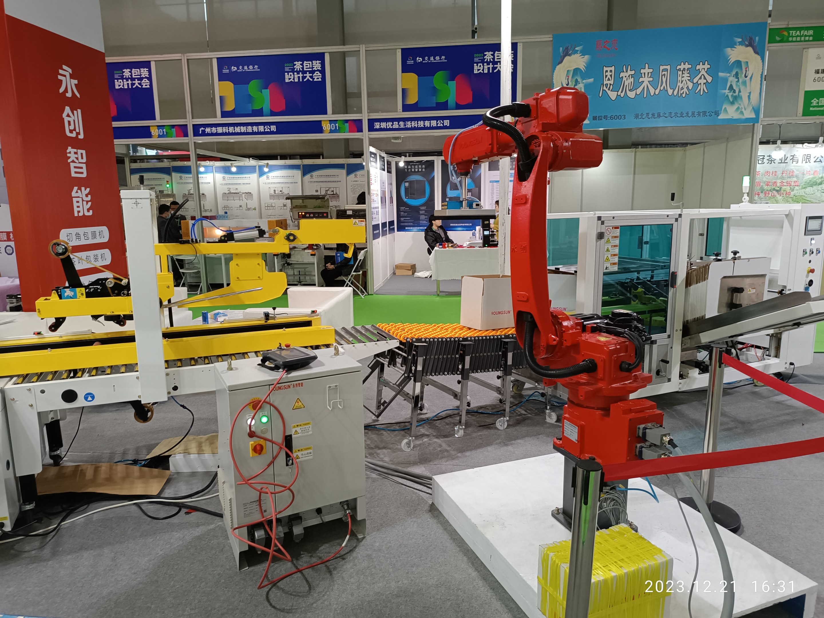 Gruppe von Robotern auf einem Tisch in einer Fabrikumgebung umgeben von Maschinen, Kabeln, Platinen und Menschen im Hintergrund.