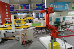 Gruppe von Robotern auf einem Tisch in einer Fabrikumgebung umgeben von Maschinen, Kabeln, Platinen und Menschen im Hintergrund.