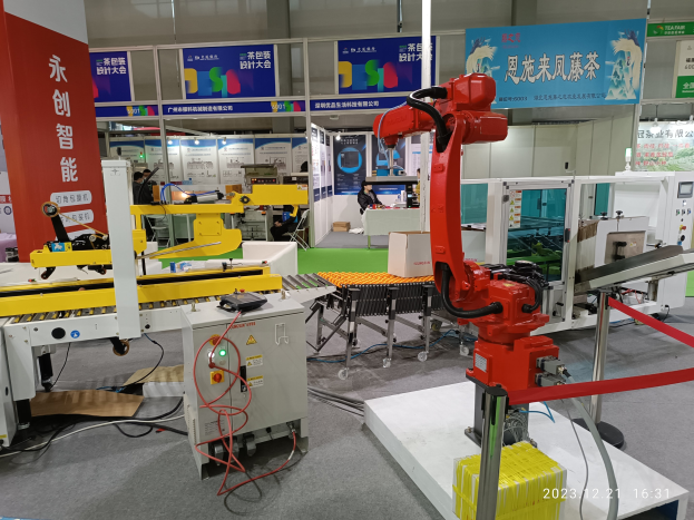 Gruppe von Robotern auf einem Tisch in einer Fabrikumgebung umgeben von Maschinen, Kabeln, Platinen und Menschen im Hintergrund.