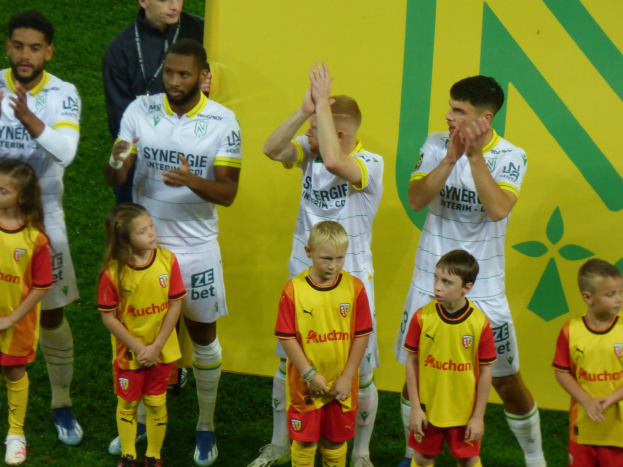 Eine Gruppe von Fußballspielern in Uniformen, die auf einem Feld mit einem "Ligue 1"-Schild im Hintergrund klatschen und einen Sieg feiern.