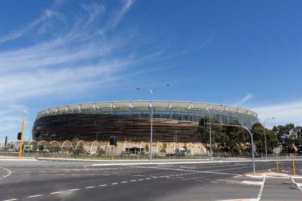 Großer Stadion mit starkem Verkehr davor, umgeben von Straßeninfrastruktur und Bäumen unter einem bewölktem Himmel.