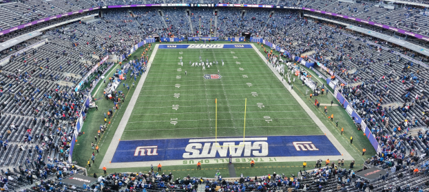 Ein volles Fußballstadion mit Spielern auf dem Feld, Torpfosten und Zuschauern auf den Tribünen unter einer lebhaften Atmosphäre.