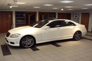 Ein weißes Auto steht in einem Raum mit Fliesenboden und Deckenbeleuchtung, mit mehreren Türen an der Rückwand sichtbar.