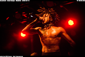 Ein Mann mit Dreadlocks singt ohne Hemd ins Mikrofon auf der Bühne, mit Text oben und unten: "scarikrd - cooler Stage - Madrid 2018-07-11".