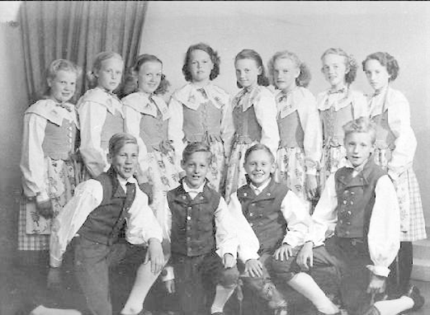 Schwarz-weiß-Foto einer Gruppe von Kindern, die vor einer Wand mit einem Vorhang posieren, beschriftet mit "1930er Kinder-Schule" unten.
